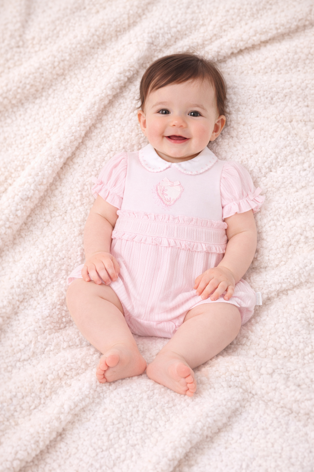 Baby in a pink outfit lying on a soft, light-colored surface