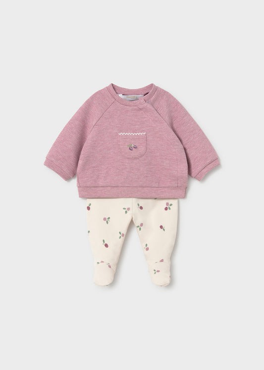 Baby outfit with pink sweatshirt and white pants on a light purple background