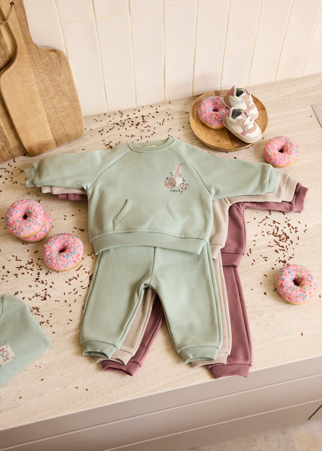 Children's green and pink outfit on a wooden surface with donuts around