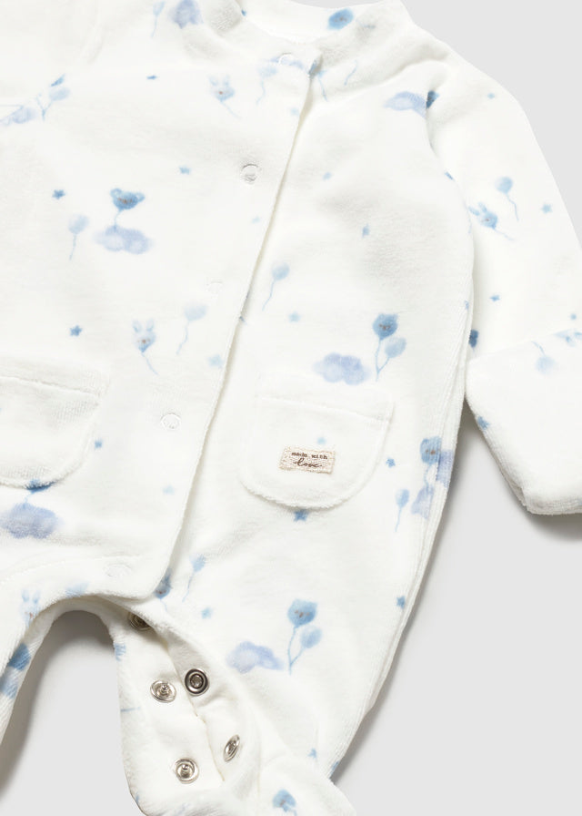 White long-sleeve baby footed romper with a light blue floral print, featuring a front snap closure, a chest pocket, and a small brand label.