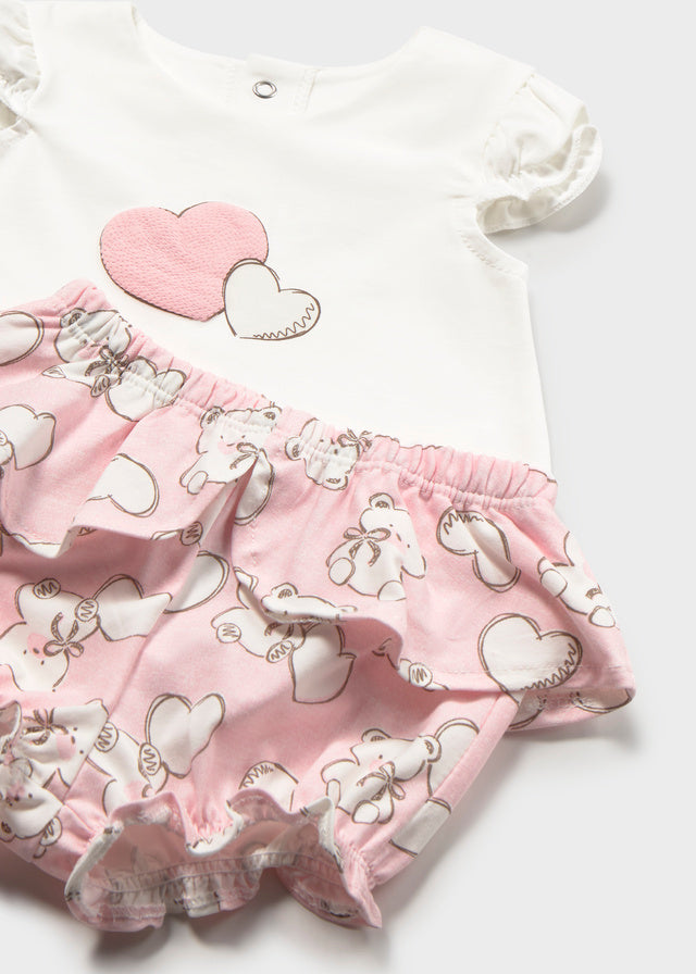 Baby outfit with pink heart-patterned shorts and white shirt on a light gray background