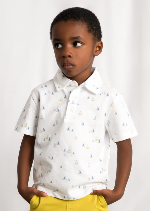 Child wearing a white polo shirt with sailboat pattern on a plain background