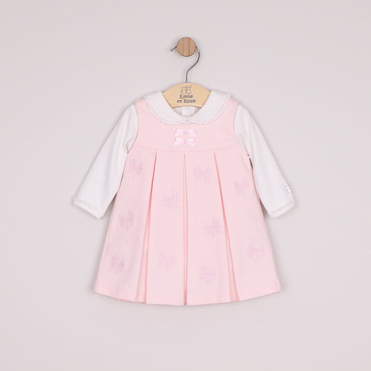 A baby girl's long-sleeve dress in light pink and white, featuring a pleated pink bodice with embroidered bow details, a white lace-trimmed collar, and a pink bow at the neckline.