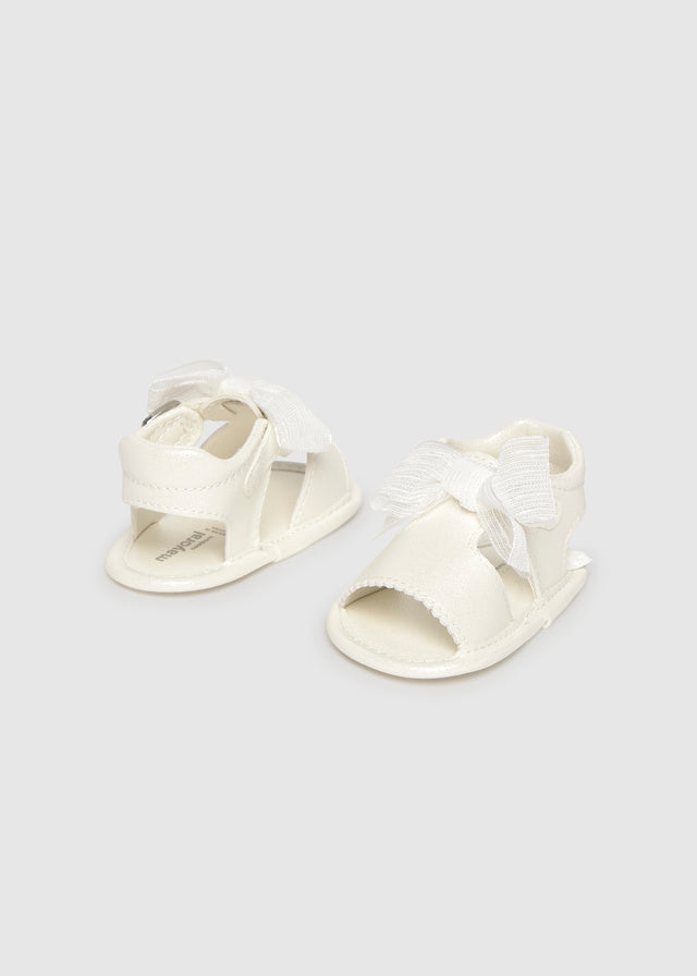 Pair of white baby sandals with bow details on a light gray background