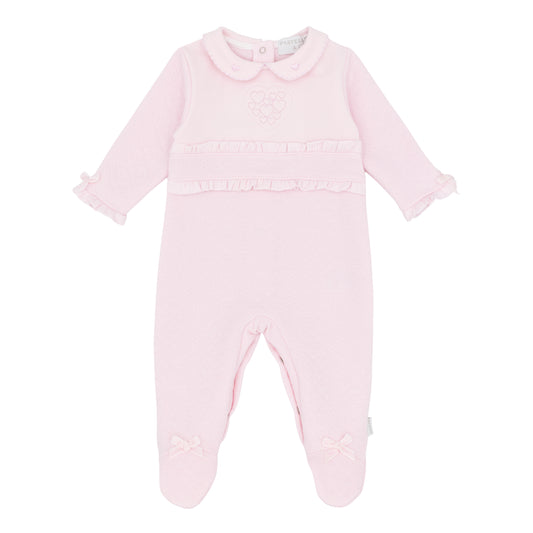 A light pink baby footed sleeper with long sleeves, a Peter Pan collar, ruffle trim at the chest and cuffs, and small bow details on the feet, shown against a plain white background.